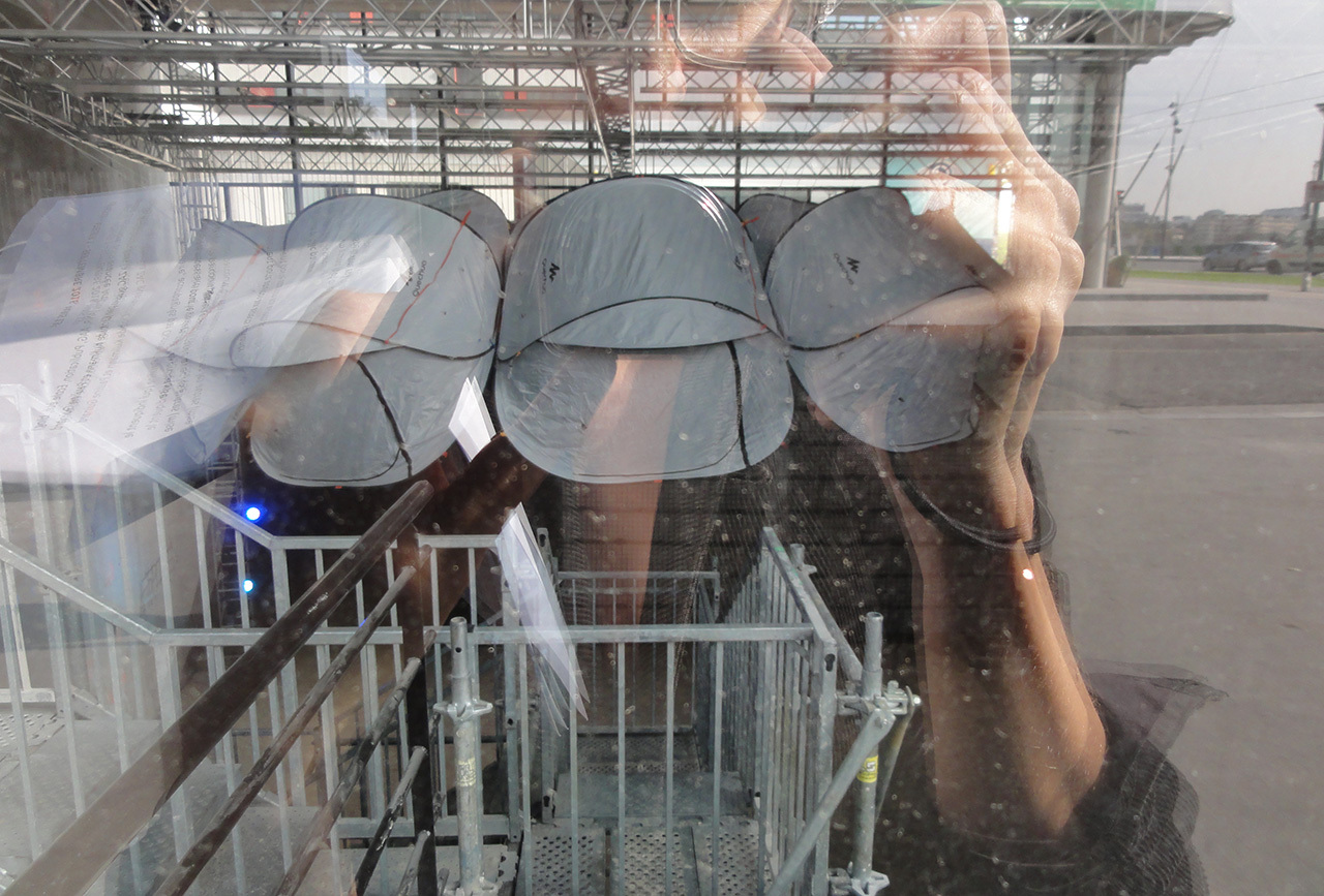 Image d'illustrationdu LAB-Deuxième groupe. Une vitre, au travers de laquelle on aperçoit des tentes dépliantes suspendues au dessus d'un escalier en métal, dans une pièce qui semble en chantier. Dans le reflet de la vitre, on perçoit la personne qui prend la photo.